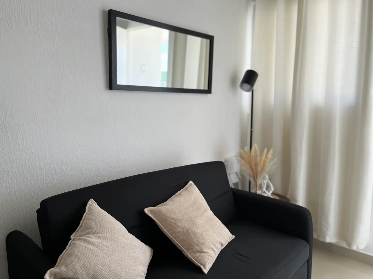 Sala de Casa Luz con sofá negro, cojines claros y espejo
