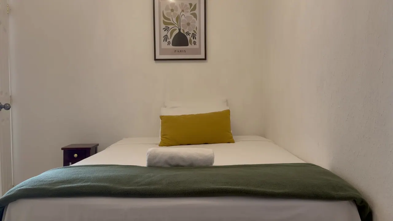 Habitación con cama, cojín mostaza y manta verde oliva